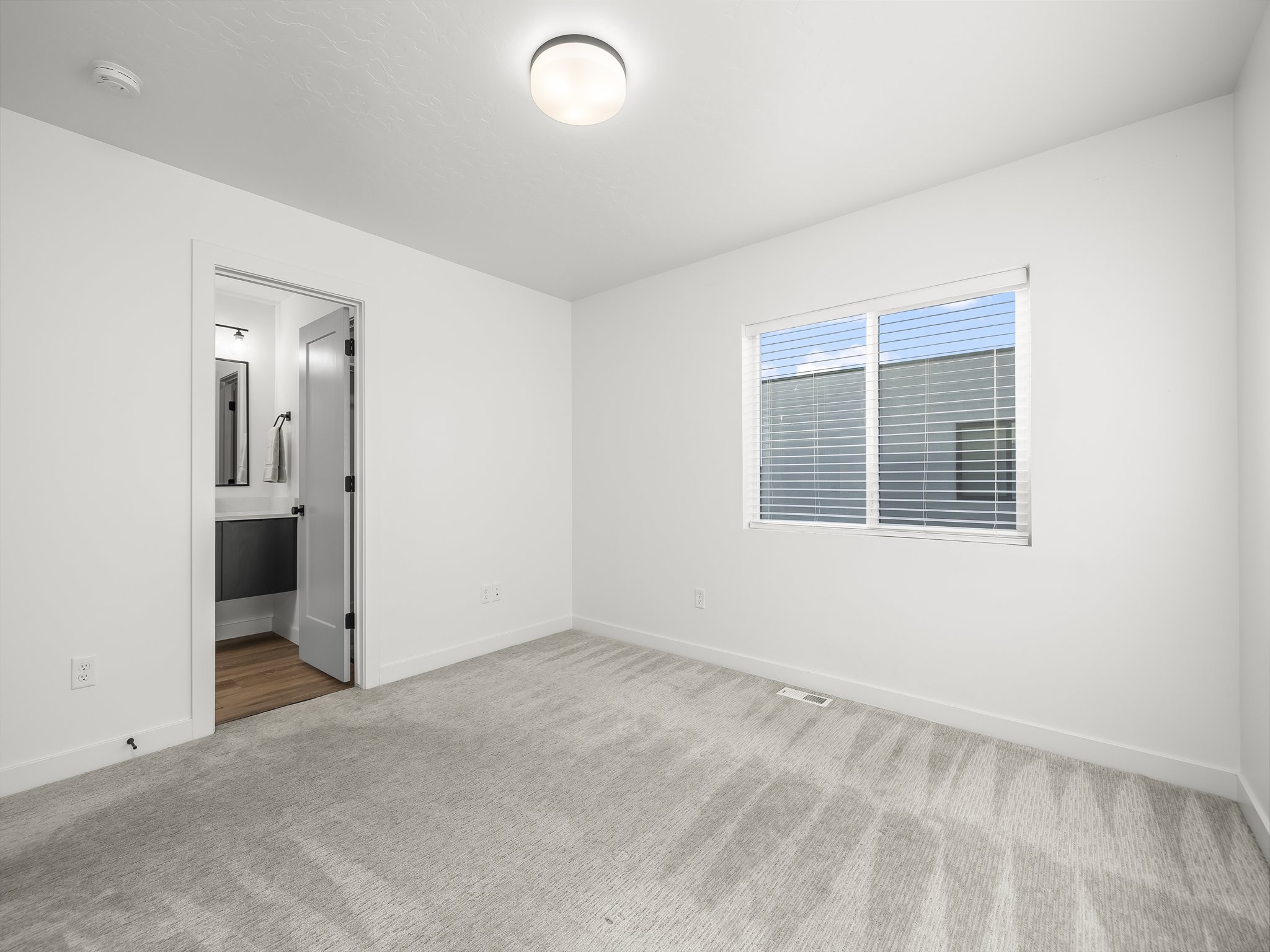 Carpeted room with white walls, a single window with blinds, and an overhead flush-mount light fixture