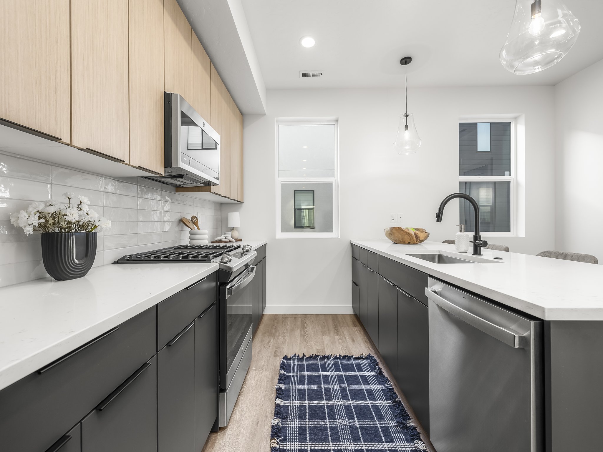 Modern kitchen featuring two-tone cabinetry with light wood-finish upper cabinets and dark lower cabinets, white countertops, and a subway tile backsplash