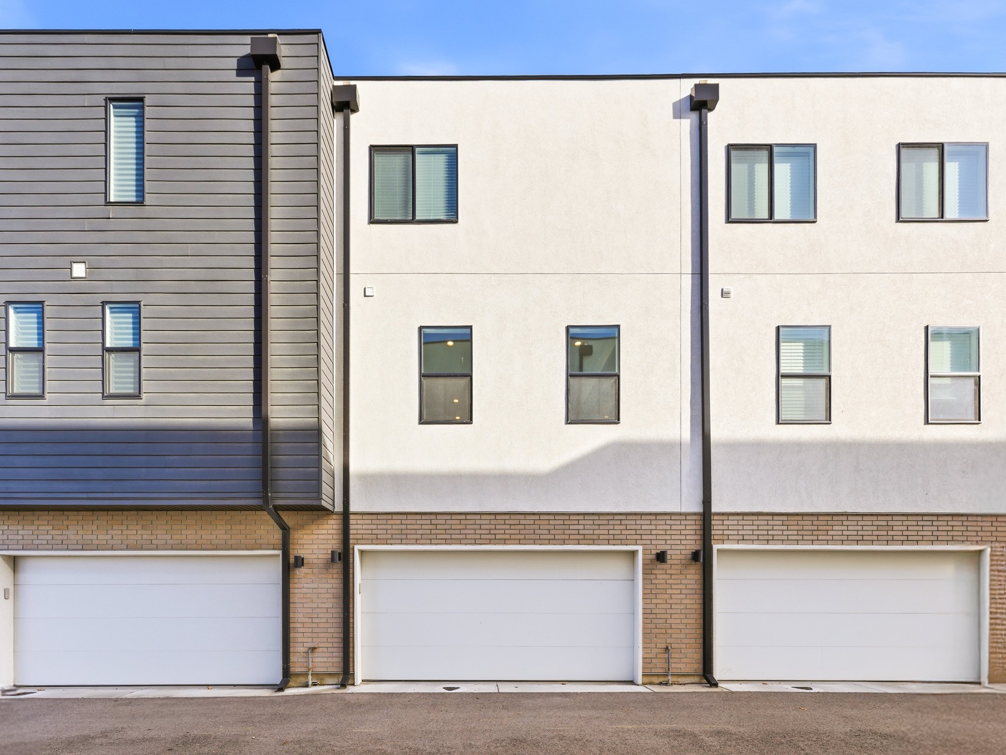 Modern multi-story facade featuring three attached garages with white doors