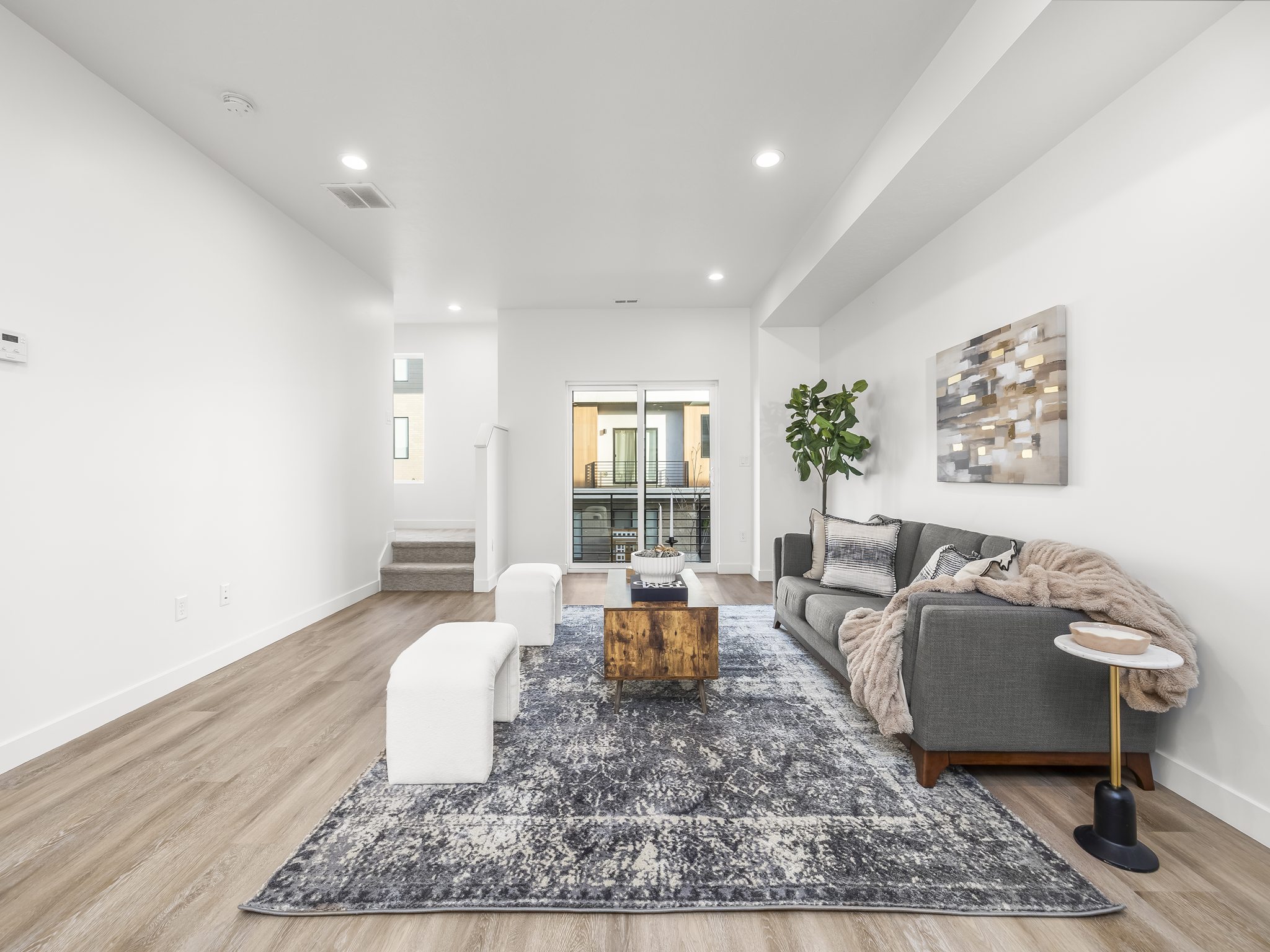 Spacious open-concept living area featuring light wood-finish flooring, recessed lighting, and a large sliding glass door