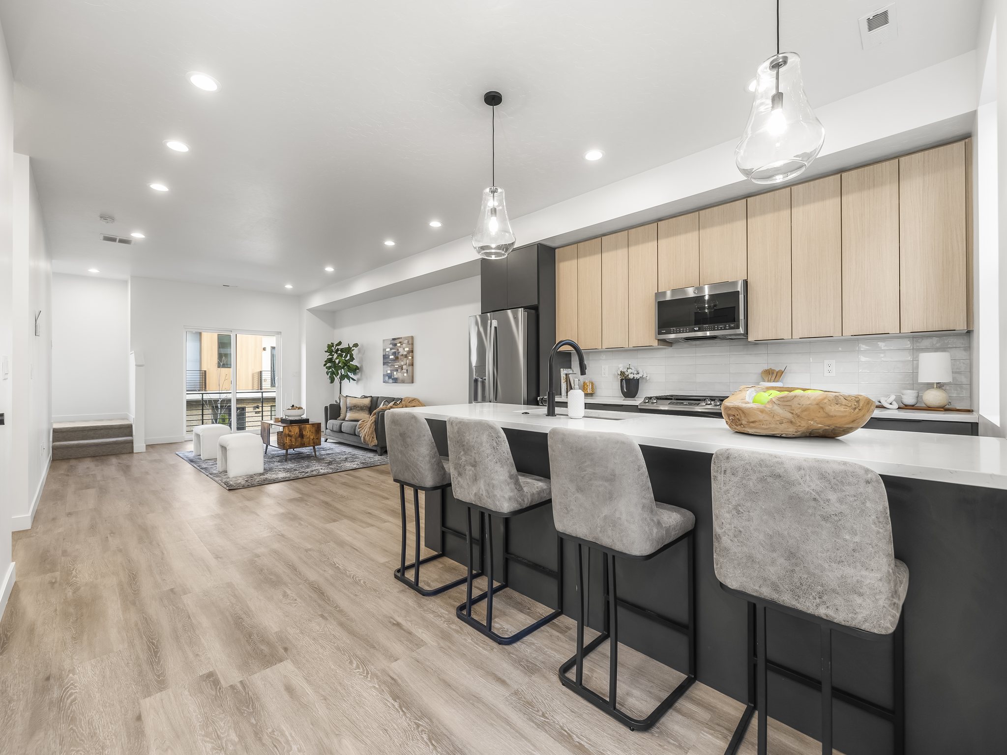 Open-concept living space featuring a contemporary kitchen with light wood-finish cabinetry, a large center island with a white countertop, and stainless steel appliances
