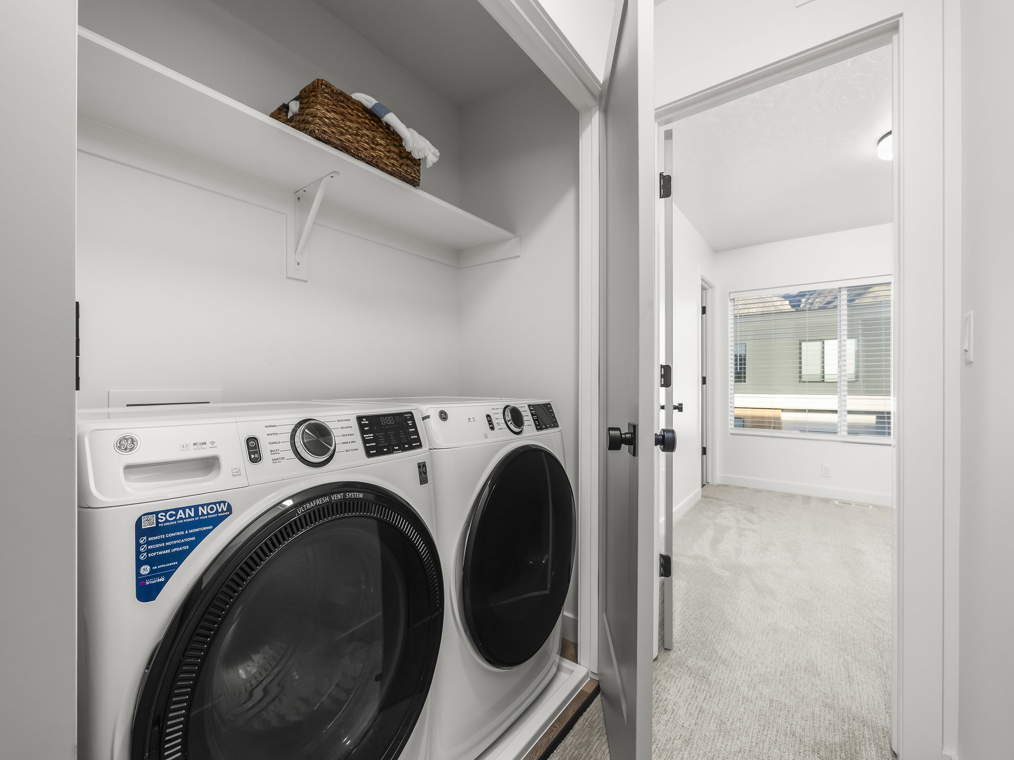 Dedicated laundry area featuring a white front-load washer and dryer set, an overhead storage shelf, and light wall finishes