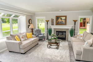 Living area featuring a stone-clad fireplace with a white mantel, large bay windows, light-toned carpeting, and crown molding