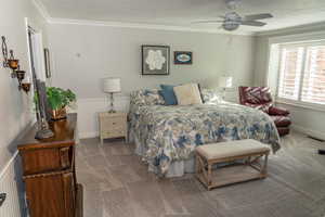 Room featuring crown molding, white wainscoting, light gray carpeting, a ceiling fan, and window shutters