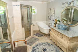 Bathroom featuring a walk-in shower with glass enclosure, a freestanding clawfoot tub, a vanity with a stone countertop and decorative vessel sink, a circular mirror, and a round window