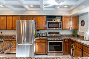 Kitchen featuring a coffered ceiling with recessed lighting, wood cabinetry, granite countertops, and stainless steel appliances