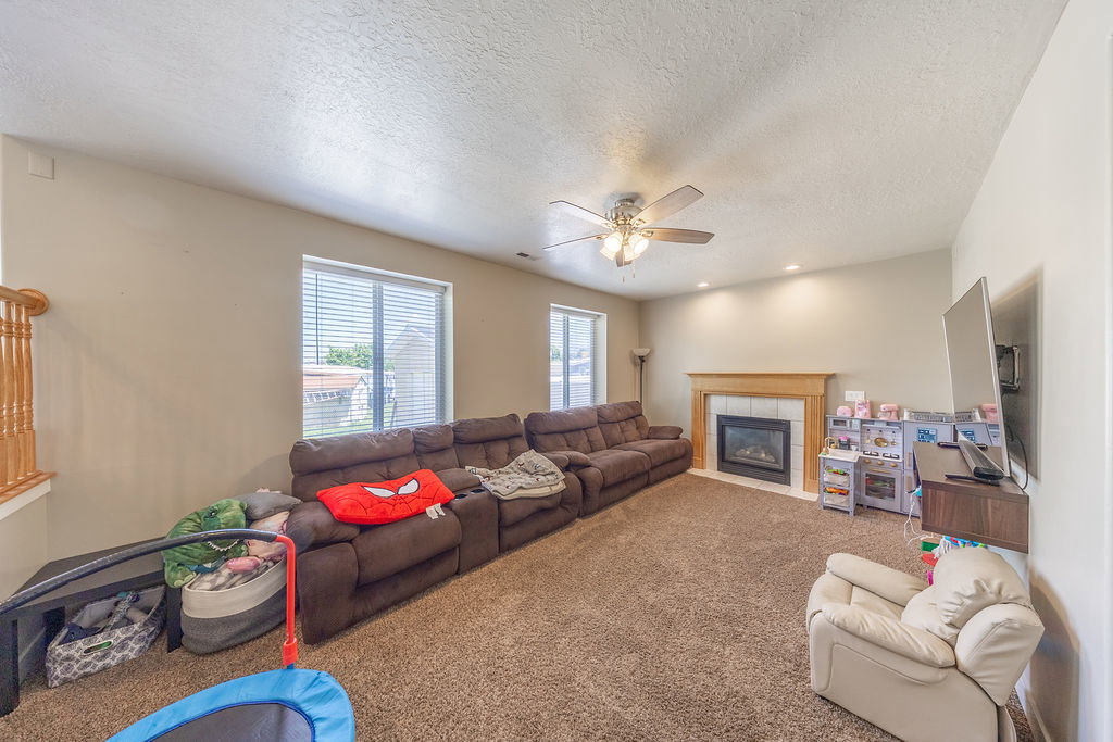 Carpeted living area featuring a fireplace with a wood mantle, recessed lighting, and a ceiling fan
