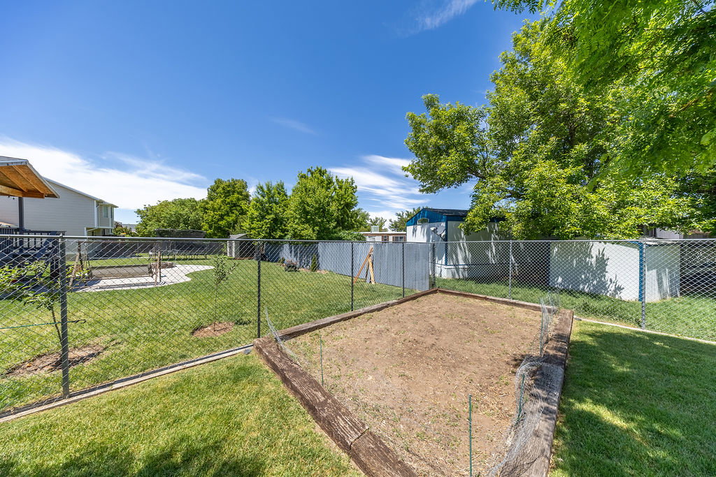 Fenced backyard featuring a large garden bed with wood borders, manicured lawn, and mature trees