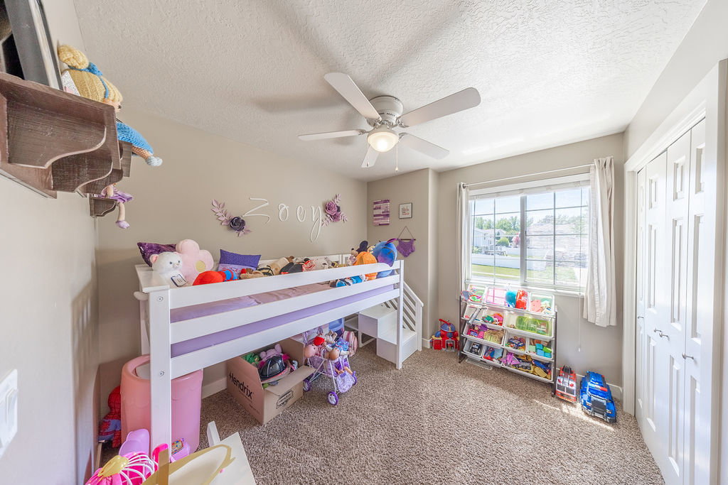 Carpeted room featuring a ceiling fan with light fixture, a window with horizontal blinds and white curtains, and a bifold door closet