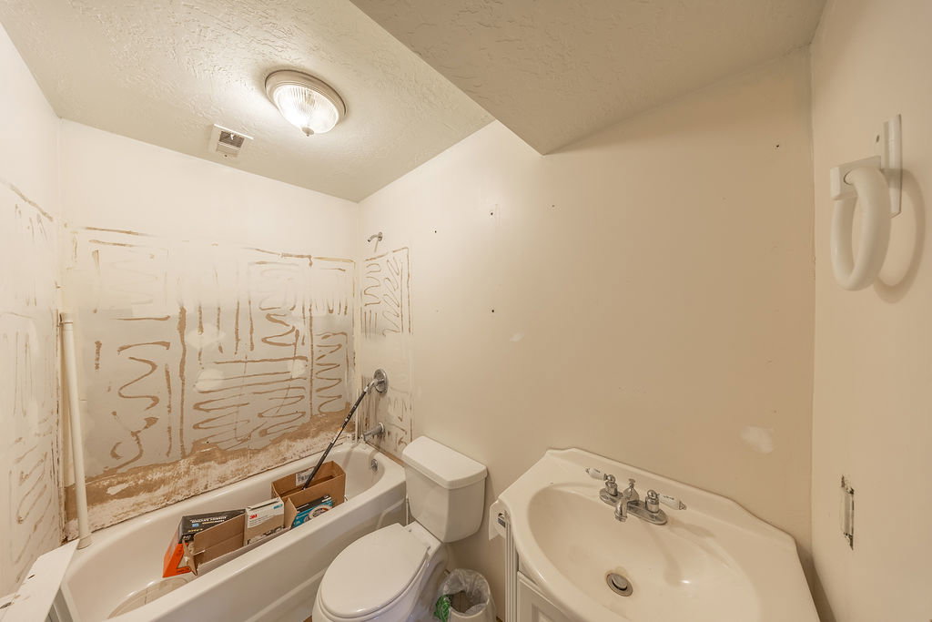 Bathroom featuring a white porcelain corner sink with chrome fixtures, a white toilet, and a white bathtub with chrome shower fixtures