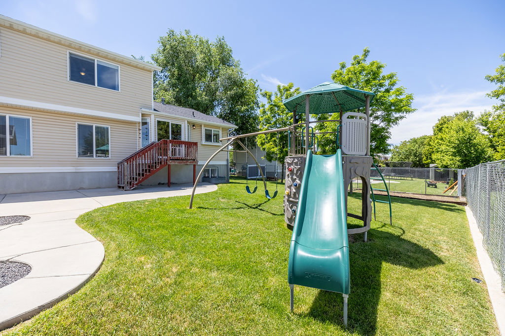 Expansive backyard featuring a green lawn, concrete patio, and a play structure with a slide and swings