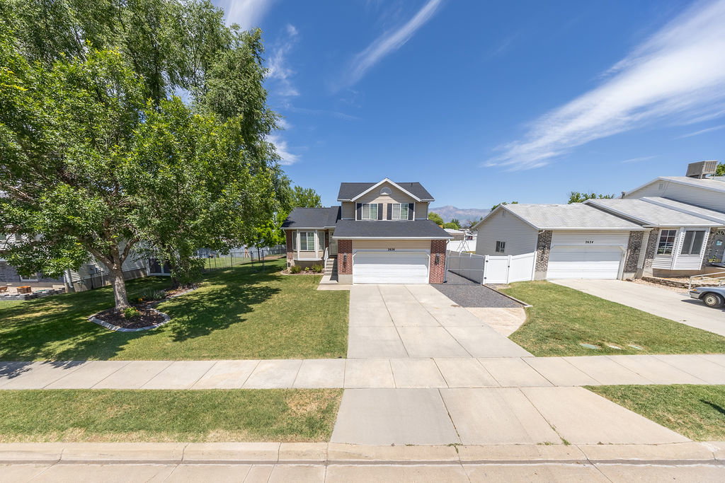 Two-story residence featuring a two-car garage, concrete driveway, and a front lawn with mature trees