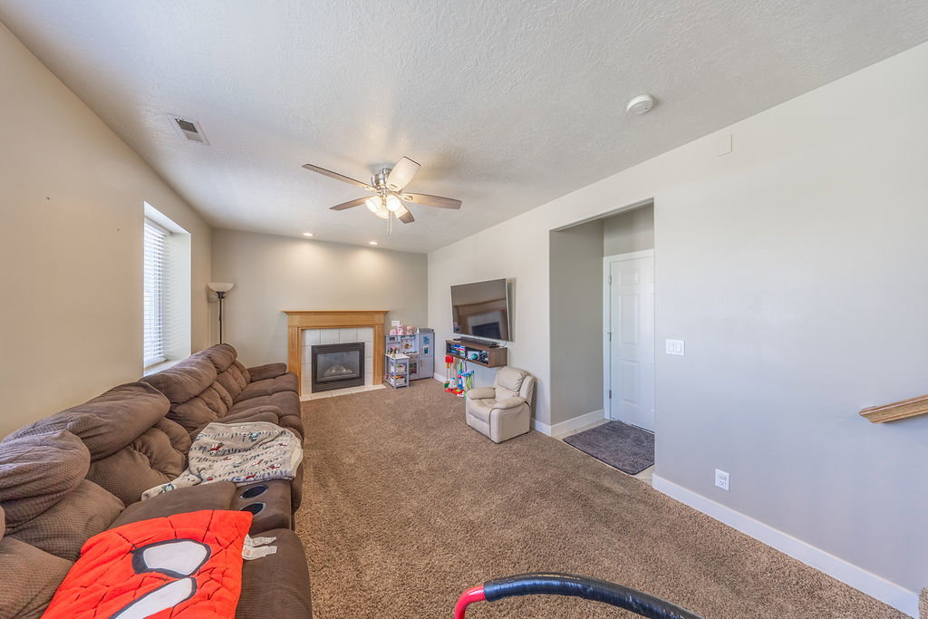 Carpeted living area featuring a fireplace with a wood mantle, recessed lighting, and a ceiling fan