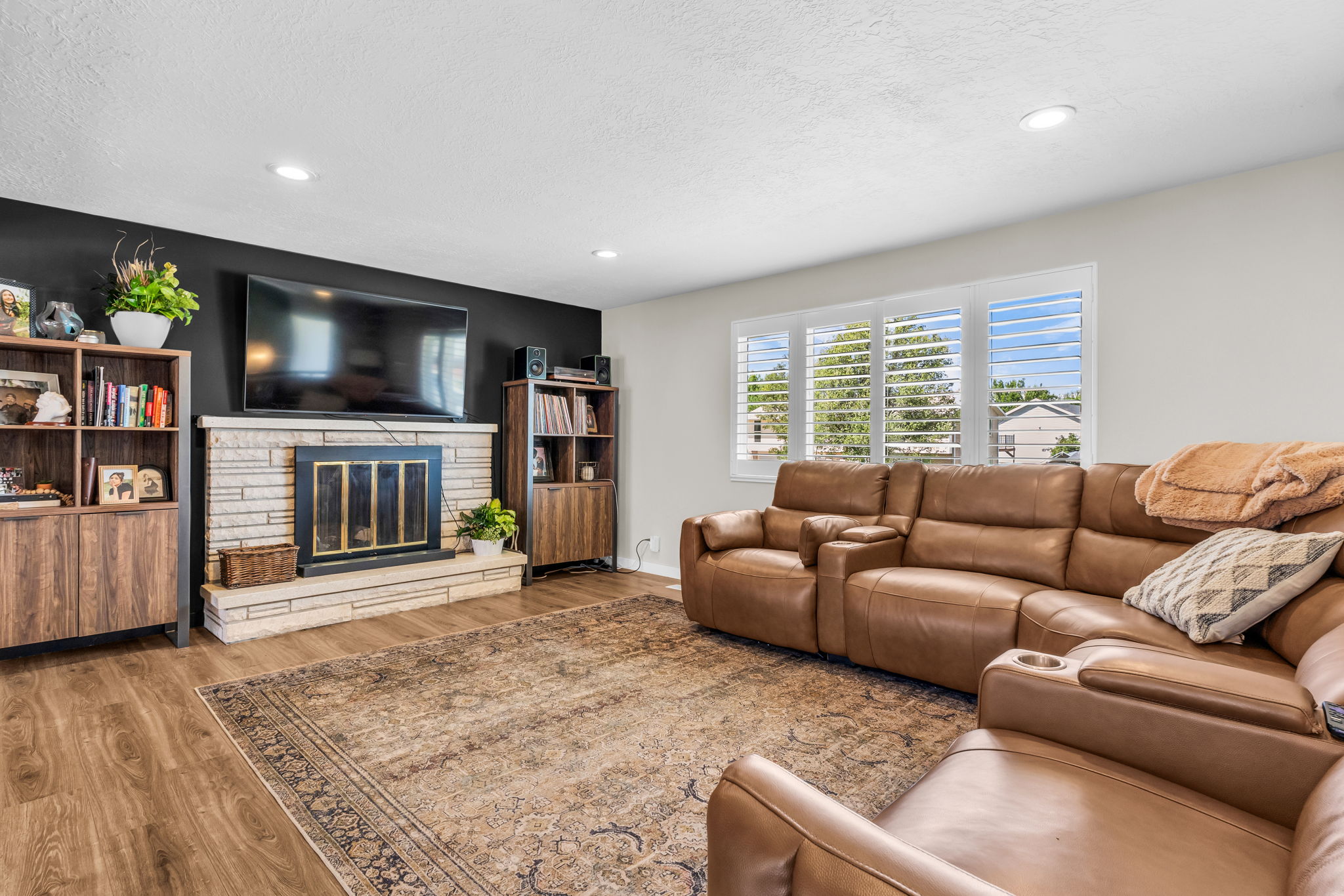 Living area featuring wood-finish flooring, a stone-clad fireplace with a black metal insert, and recessed lighting