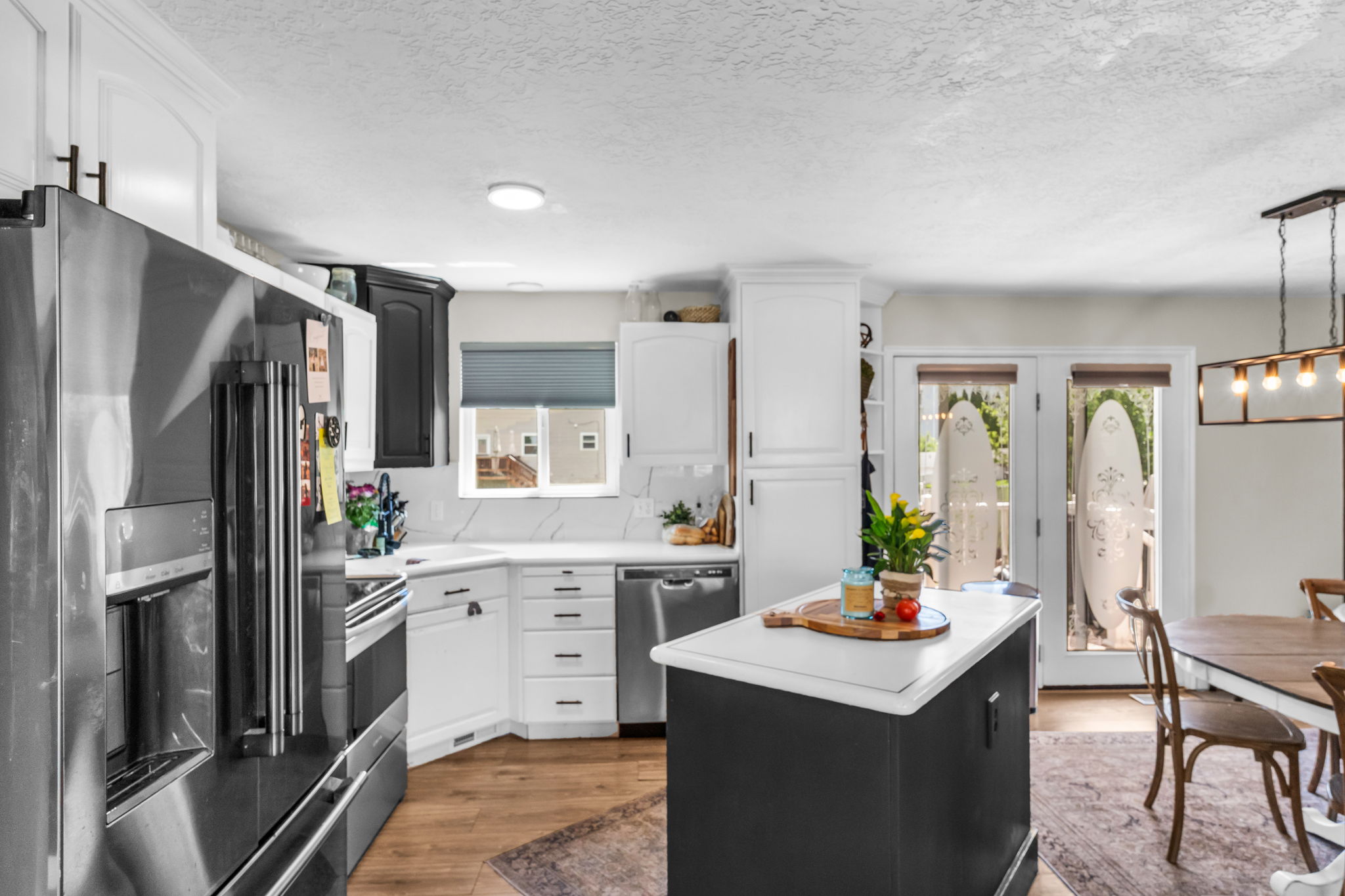 Modern kitchen featuring a stainless steel refrigerator, white cabinetry with black hardware, and wood-finish flooring
