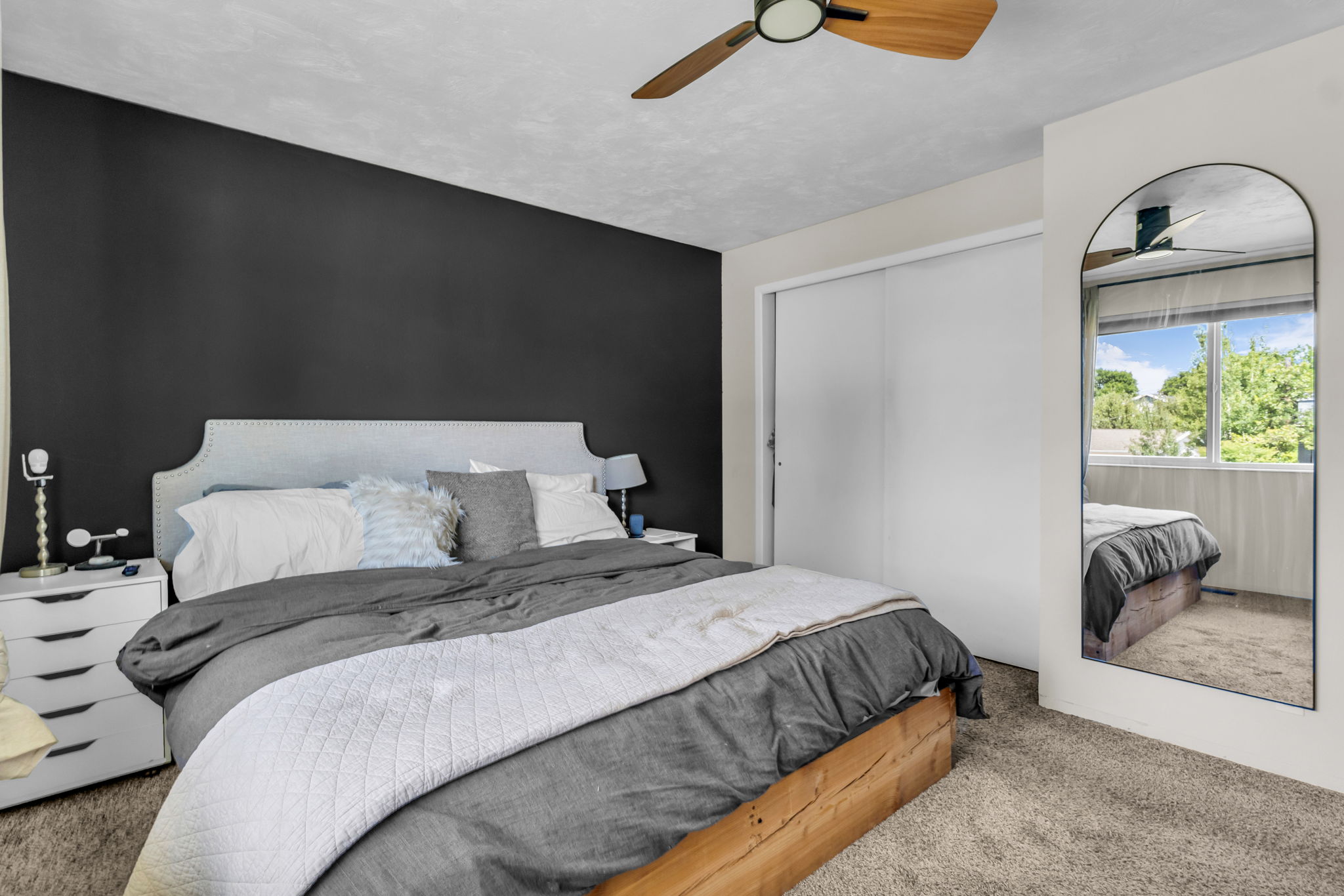 Carpeted bedroom featuring a dark accent wall, a light-toned upholstered headboard, and a ceiling fan with wood-finish blades