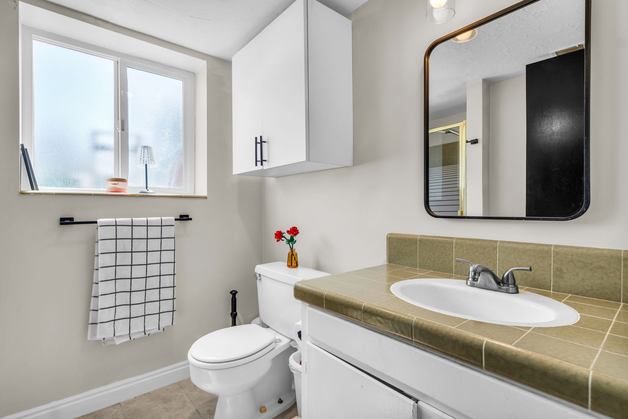 Bathroom featuring a tiled vanity with an integrated sink, a rectangular mirror with a metal frame, and a white toilet