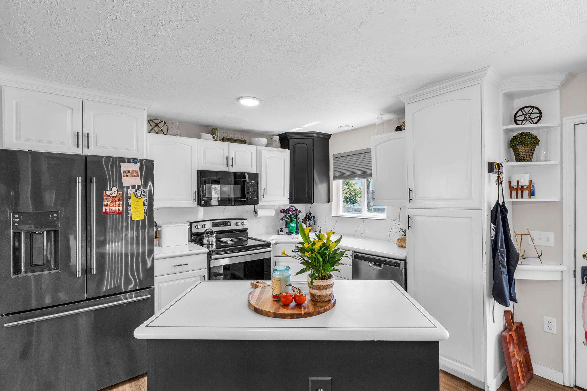 Contemporary kitchen featuring white cabinetry with black hardware, a center island with a light-colored countertop, stainless steel appliances, and a white subway tile backsplash