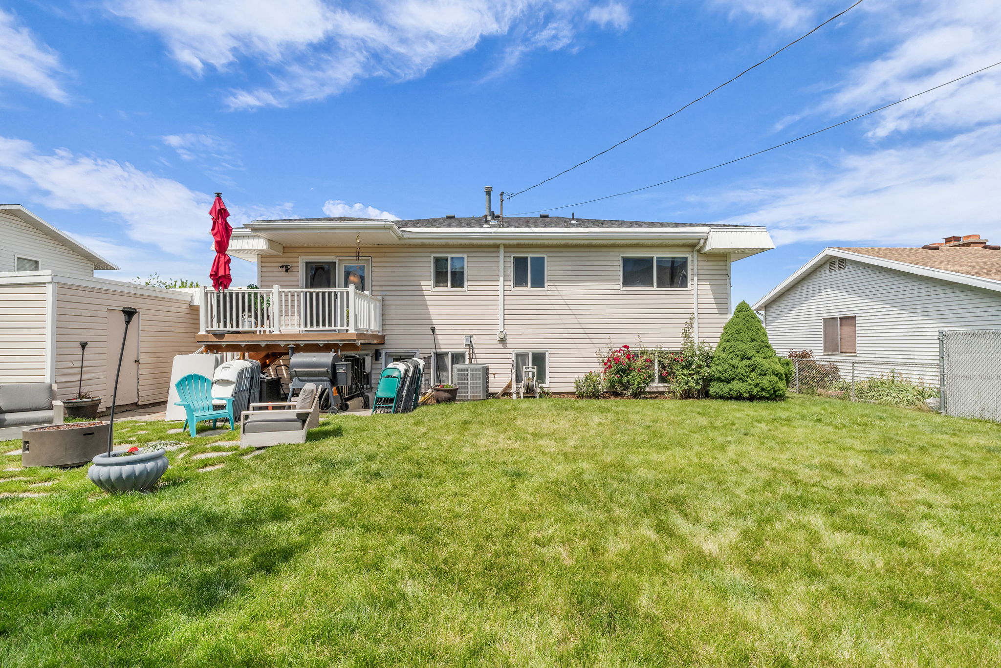 Expansive backyard featuring a green lawn, a raised wood deck with white railings, and a lower-level concrete patio
