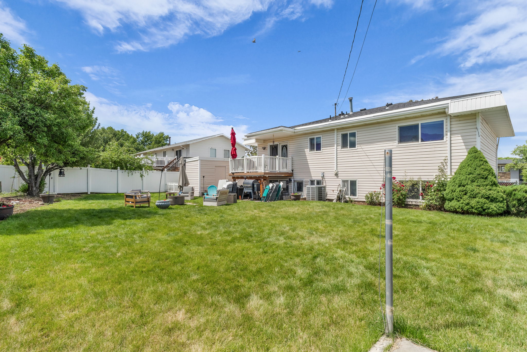 Expansive green lawn with a white privacy fence, mature trees, and a multi-level deck featuring a white railing