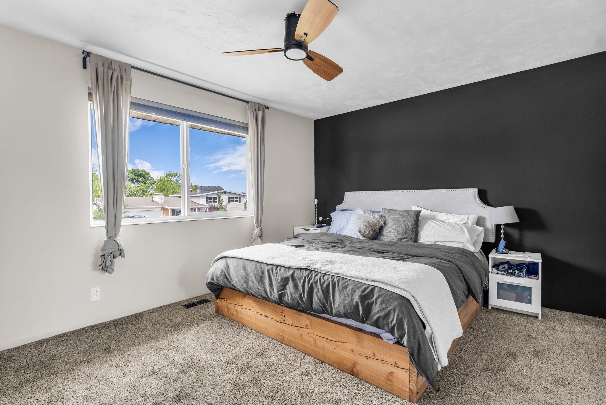 Spacious room featuring a large window, dark accent wall, and a wood-finish bed frame
