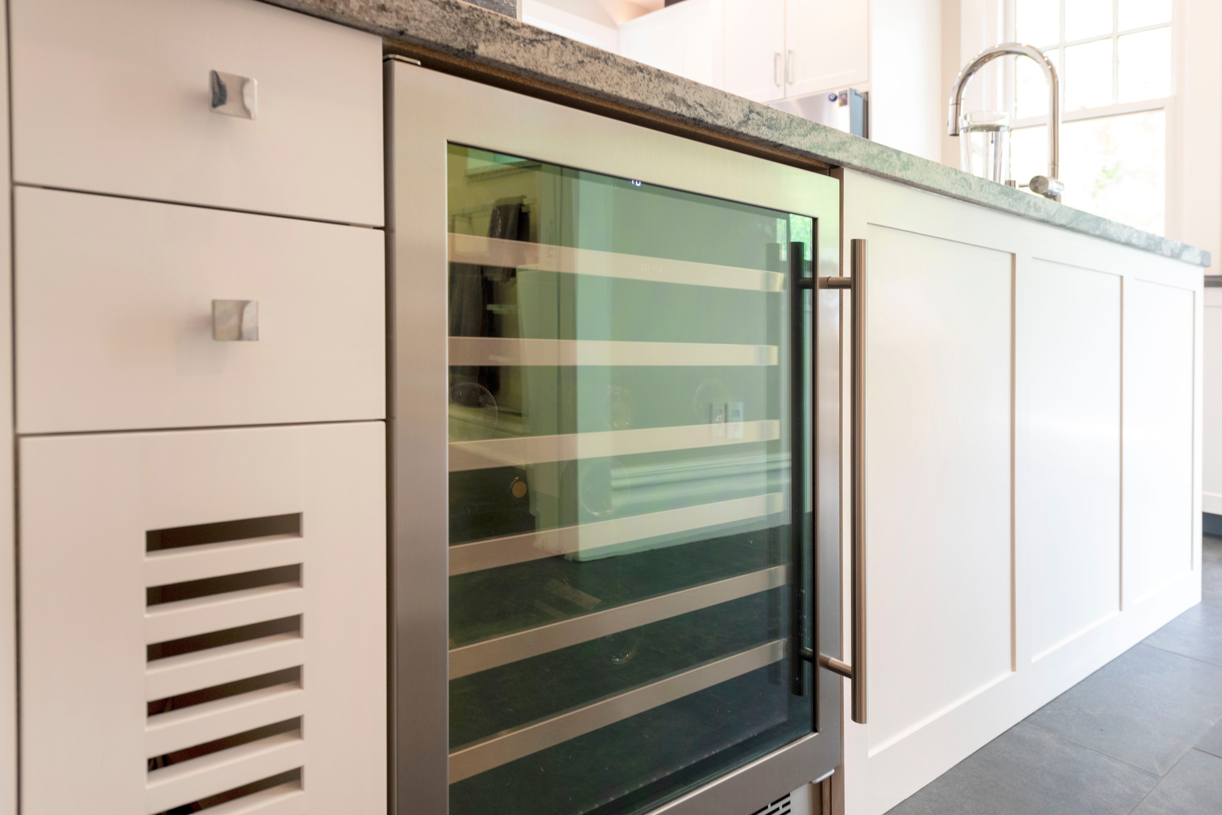 Integrated beverage refrigerator with a glass-front door, brushed metal hardware, white cabinetry, and a stone countertop