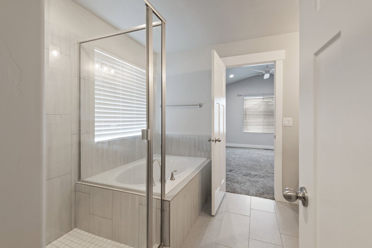 Spacious bathroom featuring a built-in tub with tile surround, a glass shower enclosure, and light-toned tile flooring