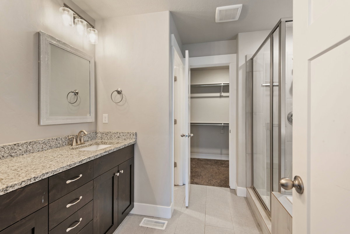 Bathroom featuring a dark wood-finish vanity with a light granite countertop, an undermount sink, and a framed mirror