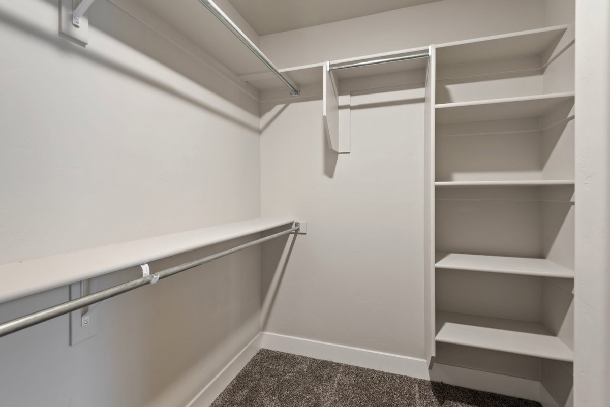 Walk-in closet featuring built-in shelving, multiple hanging rods, and dark gray carpeting