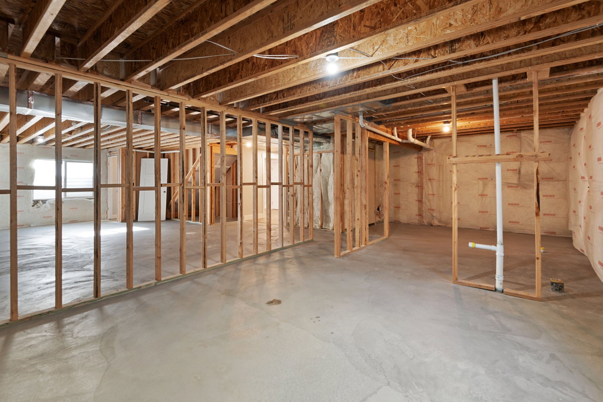 Unfinished basement featuring concrete flooring, exposed wooden joists and framing, and a window opening