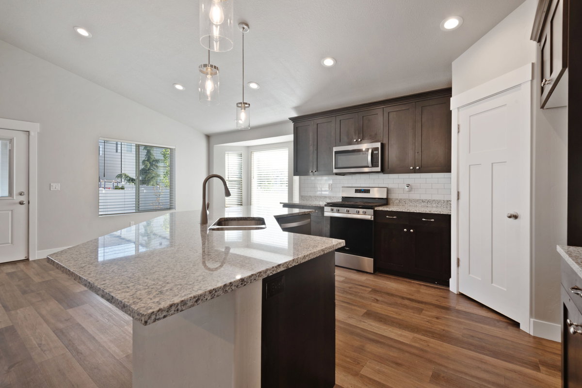 Kitchen featuring wood-finish flooring, dark wood cabinetry, stainless steel appliances, and an island with a light speckled countertop and integrated sink