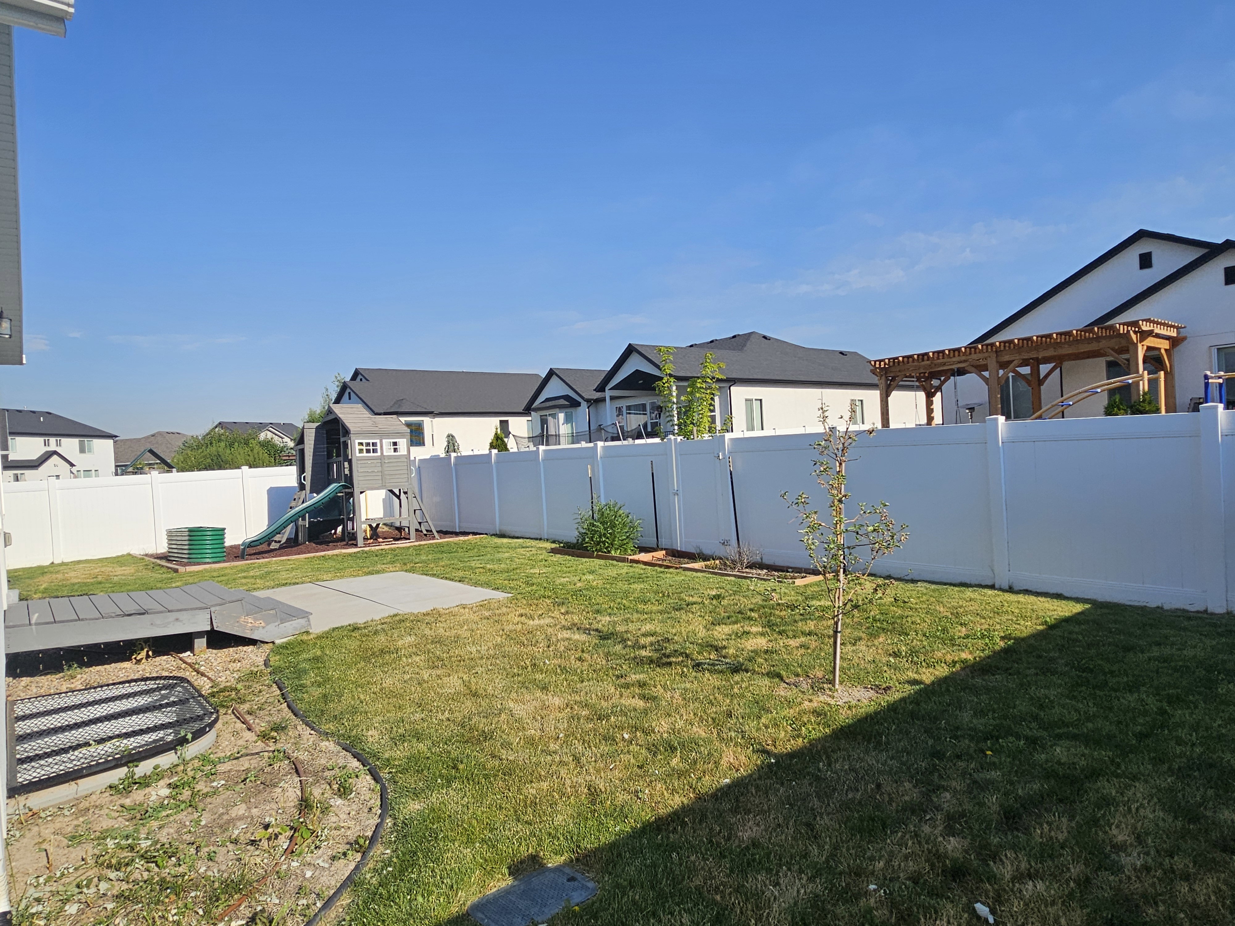 Expansive backyard featuring a manicured lawn, a concrete patio area, and a white vinyl privacy fence