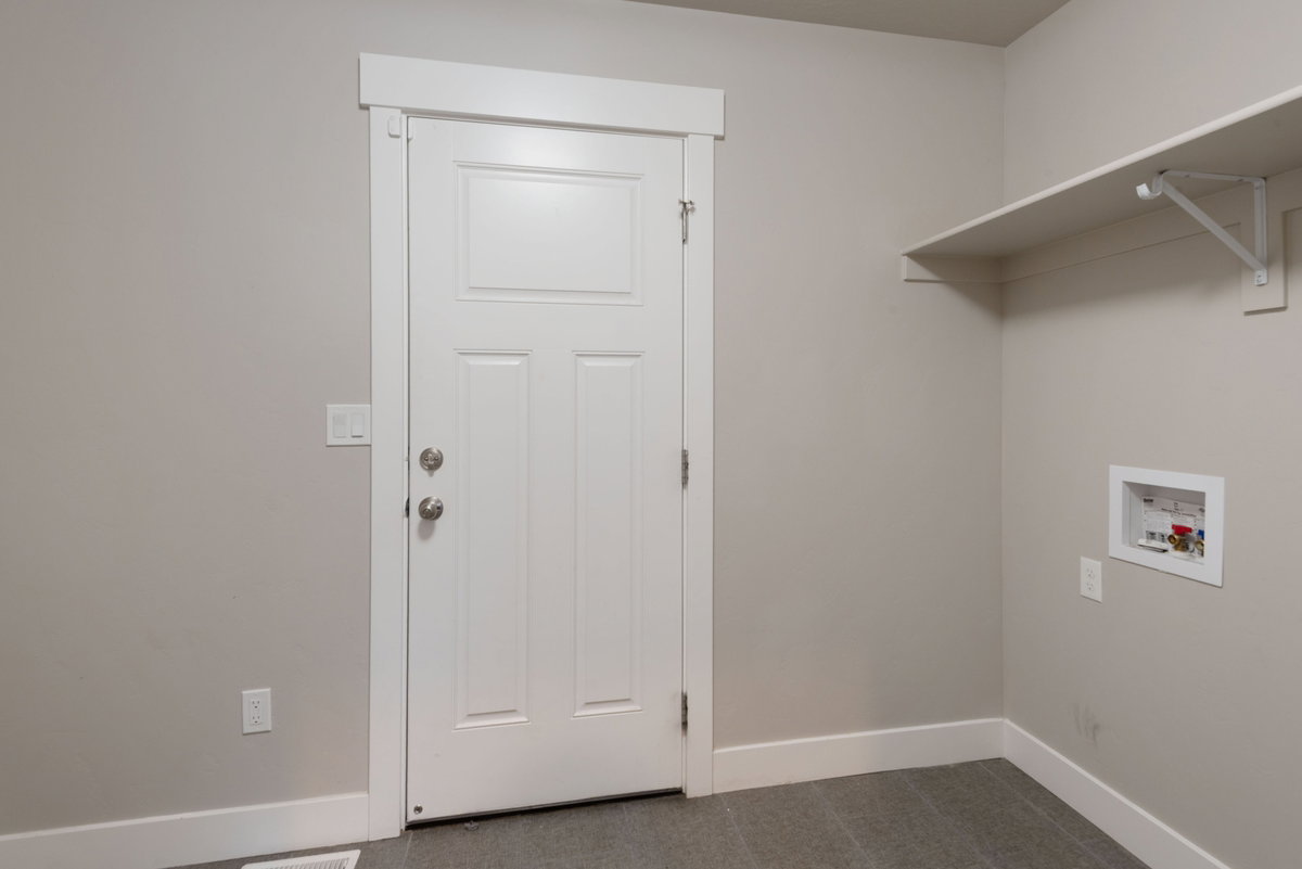 Utility room featuring a white paneled door, light gray walls, white baseboards, and a built-in white shelf
