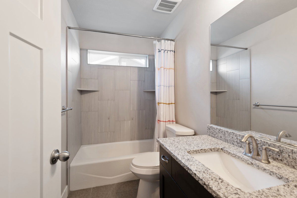 Bathroom featuring a granite countertop vanity with an undermount sink, a large mirror, and a bathtub with tiled surround