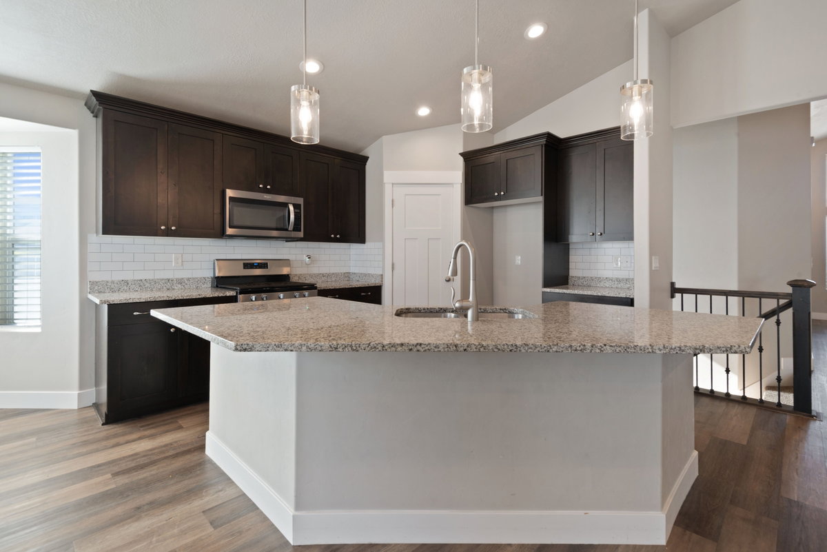 Kitchen featuring a large central island with a sink, granite countertops, dark wood cabinetry, stainless steel appliances, and wood-finish flooring