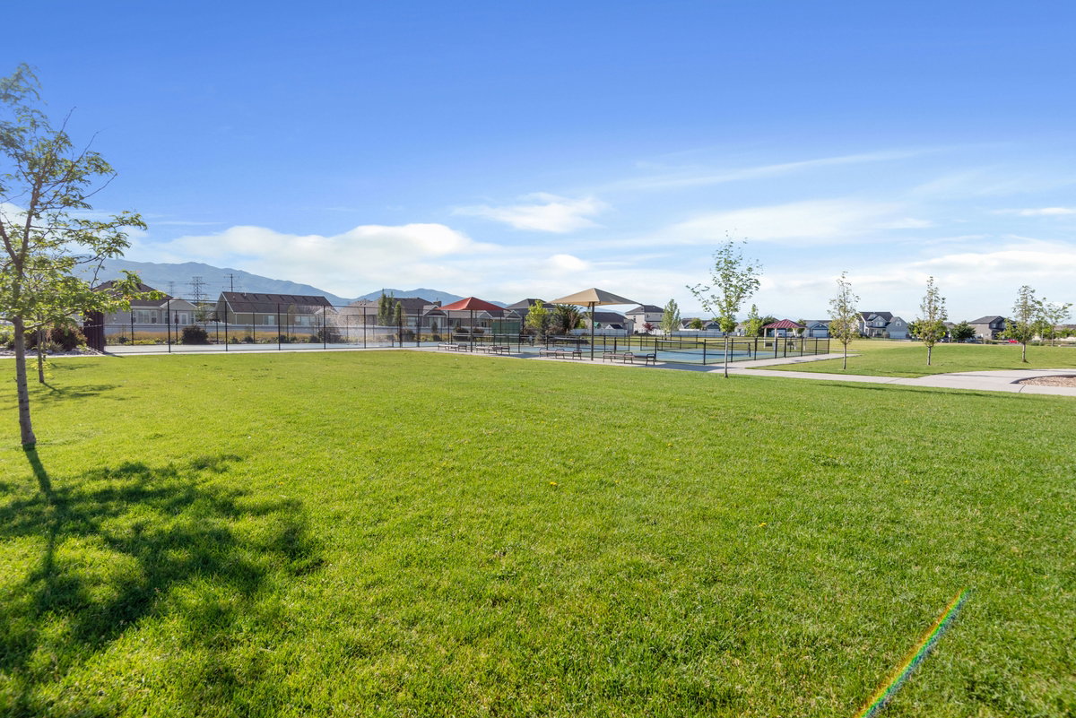 Expansive green space featuring a paved walkway, mature trees, and a distant mountain range