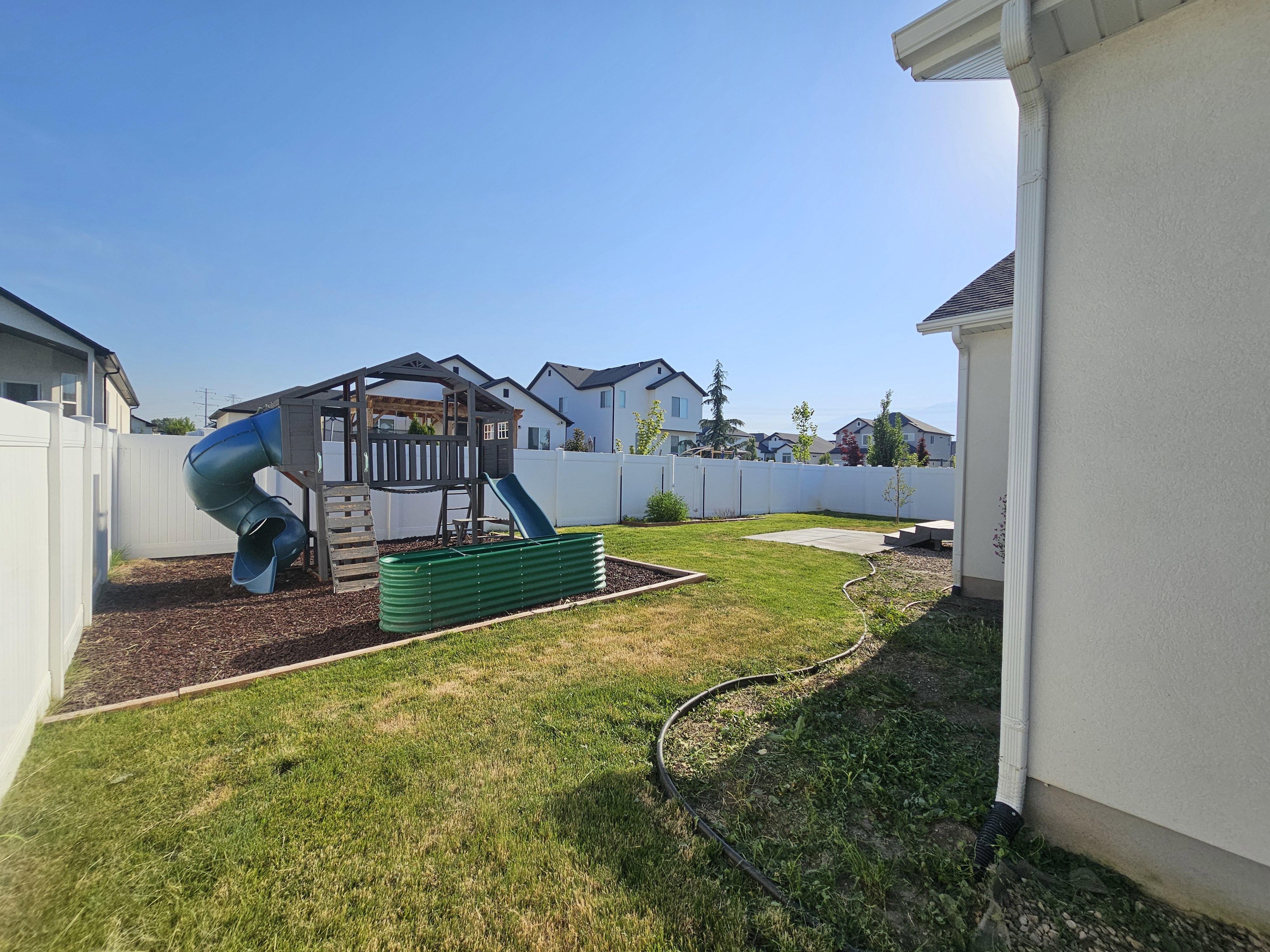 Spacious backyard featuring a manicured lawn, white vinyl fencing, and a concrete patio