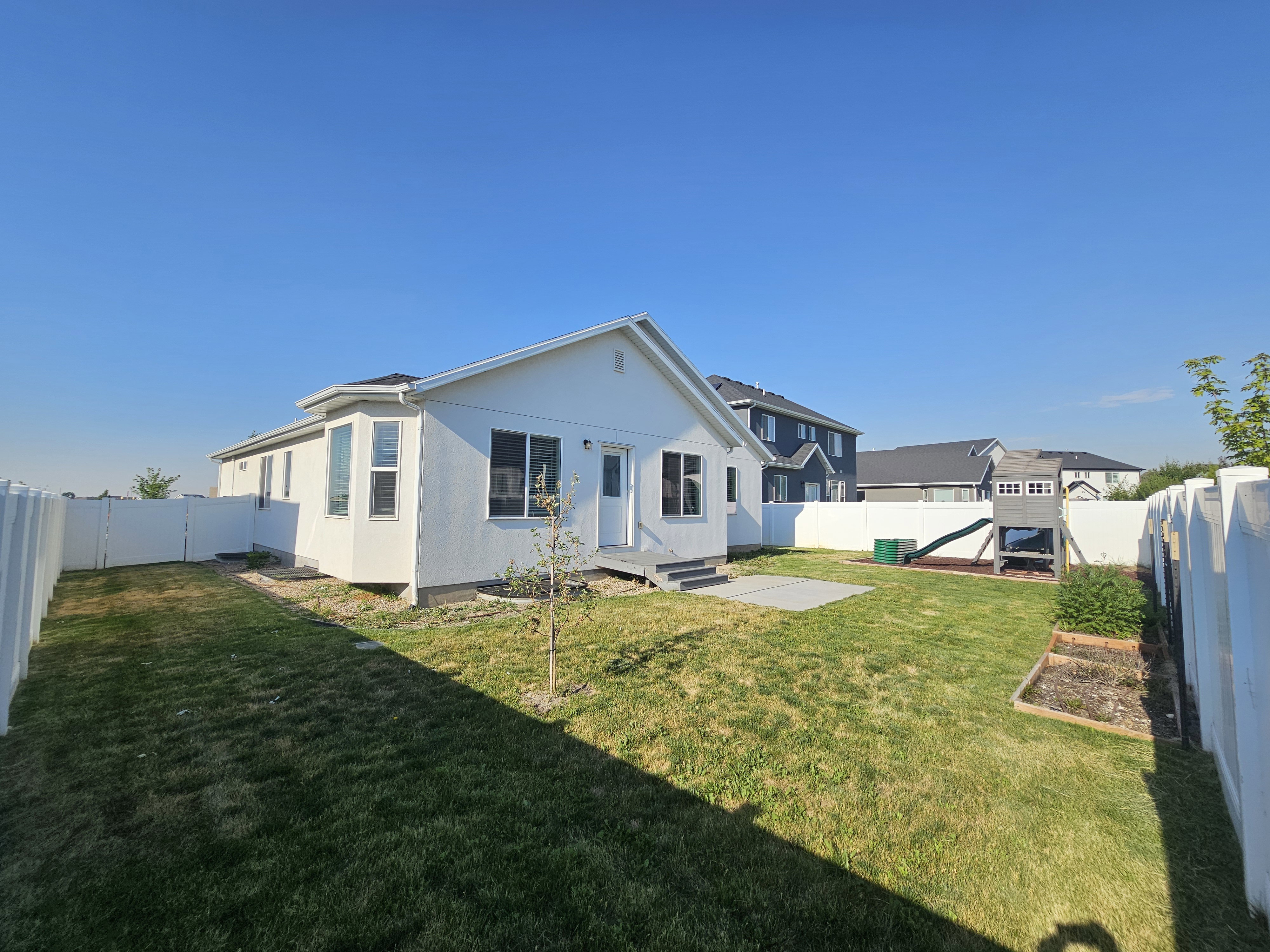Expansive backyard featuring a manicured lawn, white privacy fencing, a concrete patio area, a bay window, and a rear entry door