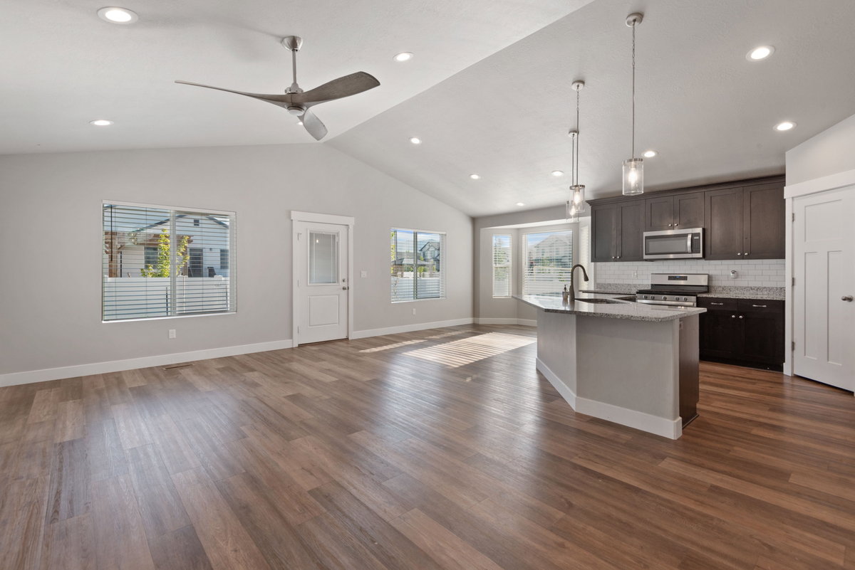 Open-concept living area featuring wood-finish flooring, vaulted ceilings, recessed lighting, a modern ceiling fan, and a kitchen with dark cabinetry, stainless steel appliances, and a central island with pendant lighting