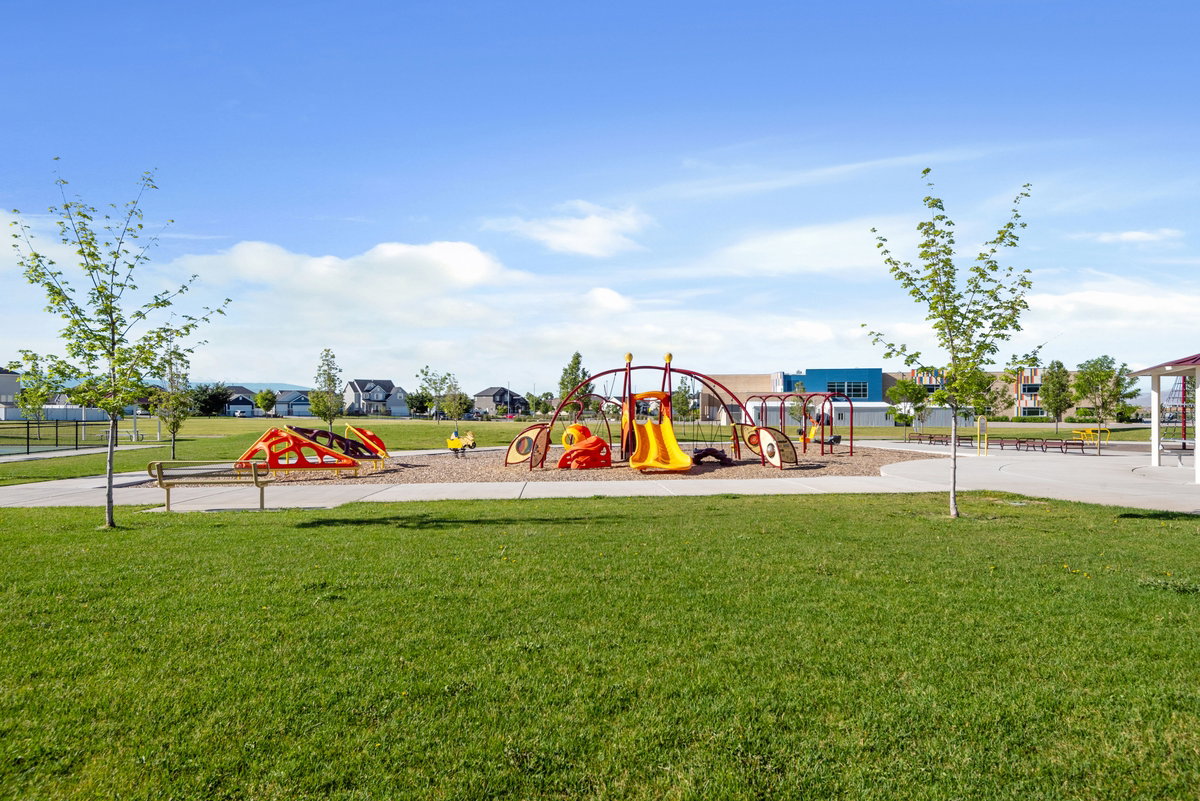 Expansive green space featuring playground equipment, a paved walkway, and scattered young trees