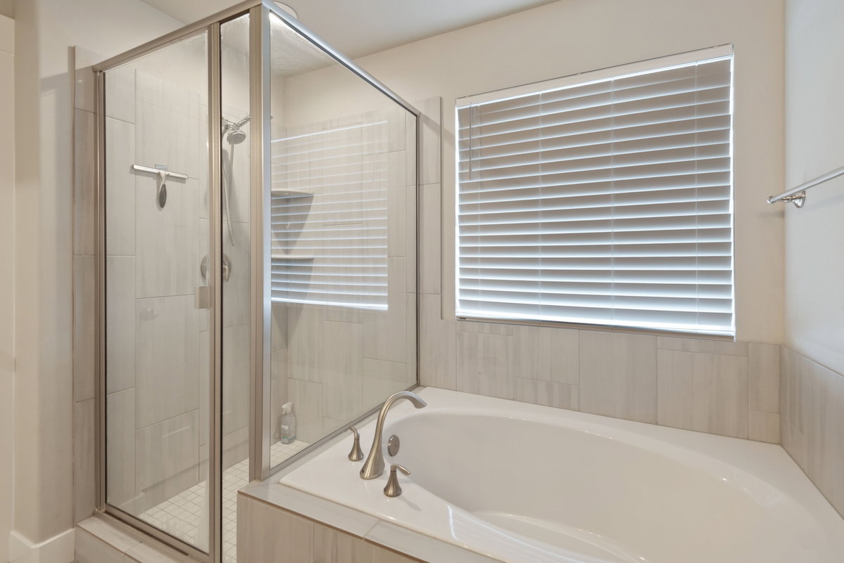 Spacious bathroom featuring a built-in soaking tub with brushed nickel fixtures, a glass-enclosed shower with subway tile surround, and a privacy window with horizontal blinds