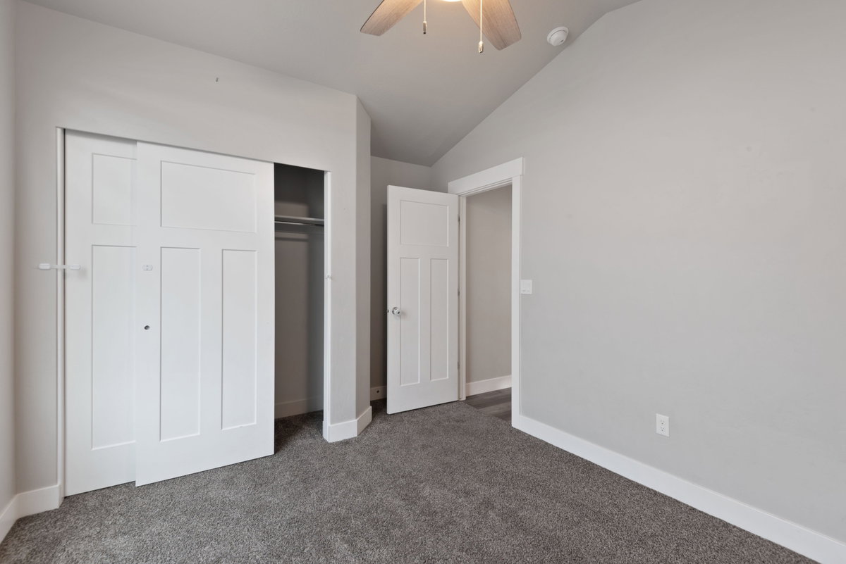 Bedroom featuring a vaulted ceiling with a ceiling fan, plush carpet flooring, white trim, and a closet with sliding panel doors