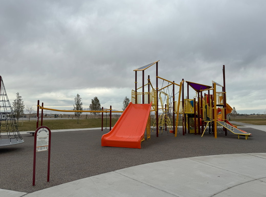 Community playground featuring a large multi-level play structure with slides, climbing elements, and overhead shade canopies