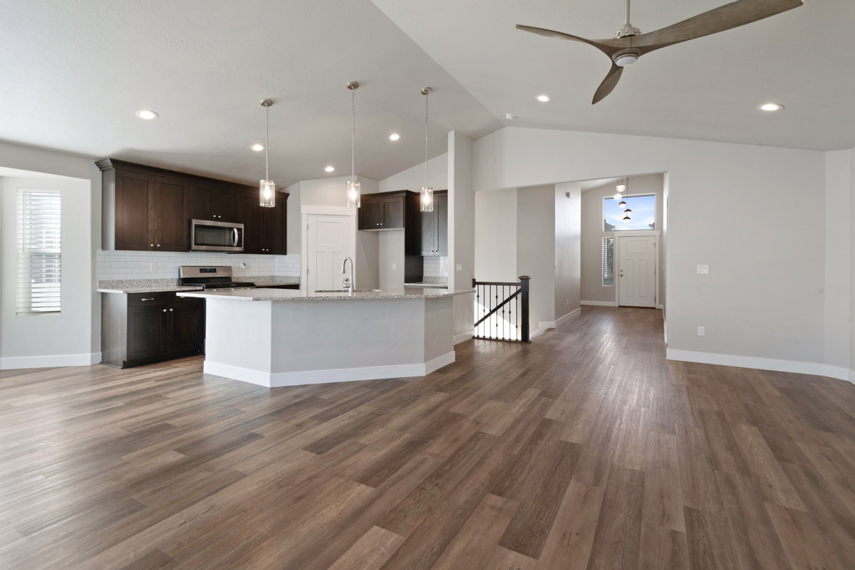 Open-concept living space featuring wood-finish flooring, a modern kitchen island with pendant lighting, dark wood cabinetry, and stainless steel appliances