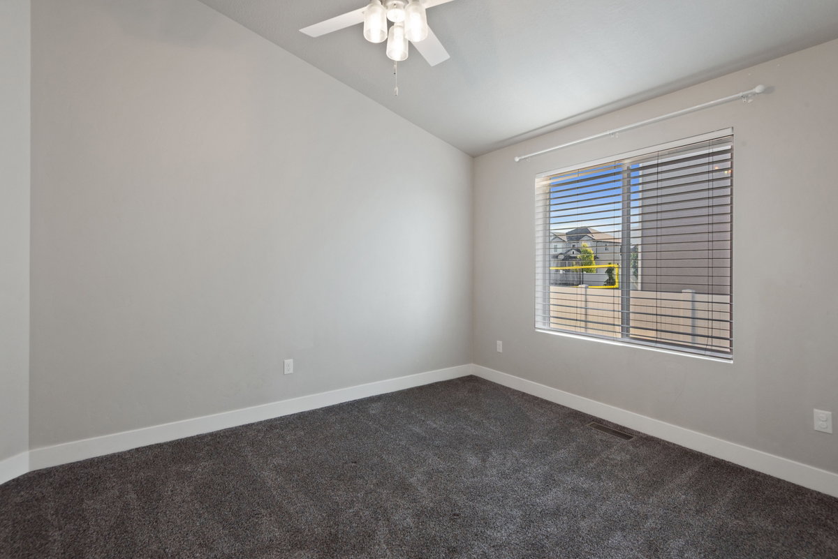 Room featuring neutral wall paint, dark grey carpeting, a large window with horizontal blinds, and a white ceiling fan with light fixture