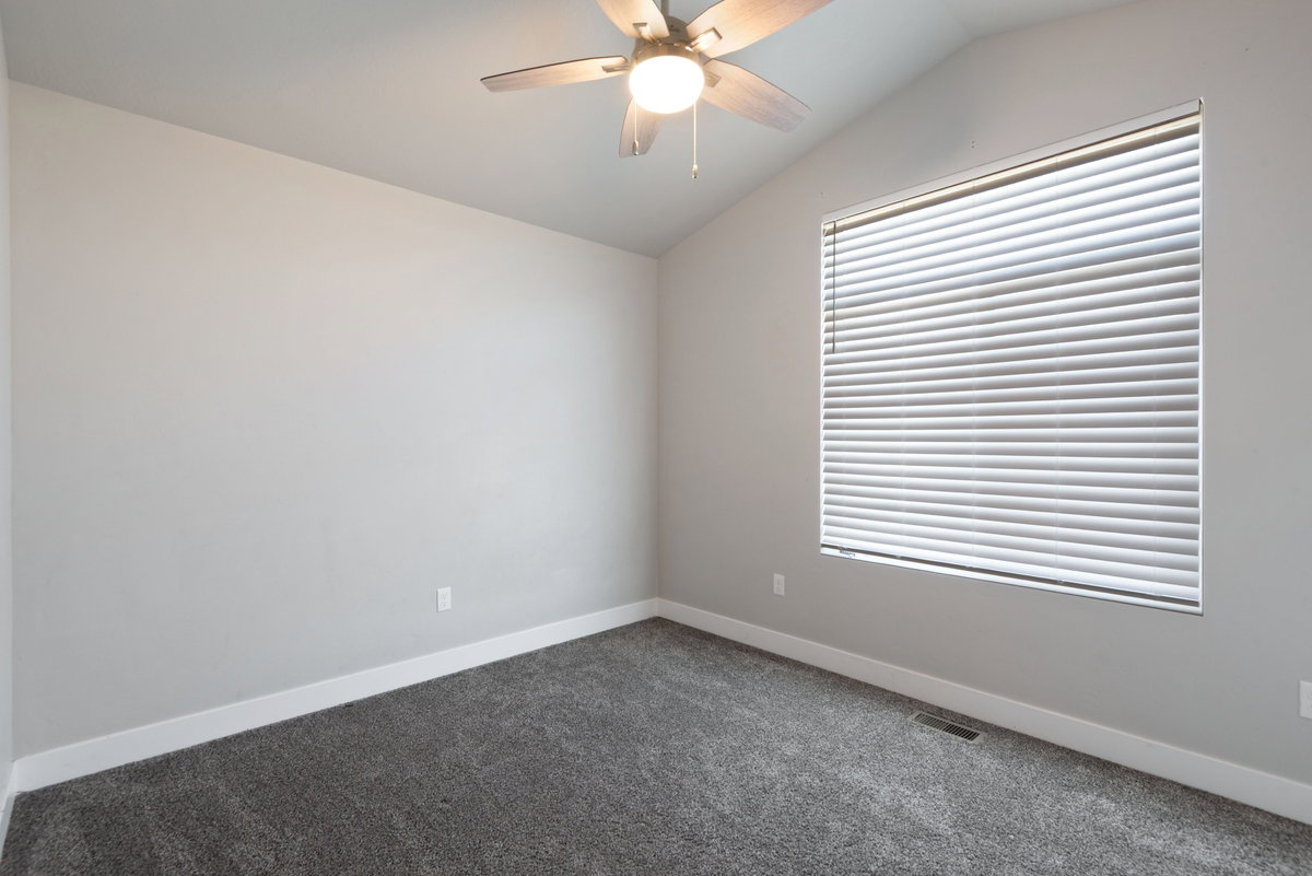Room featuring a window with horizontal blinds, vaulted ceiling, ceiling fan with integrated lighting, and gray carpeting