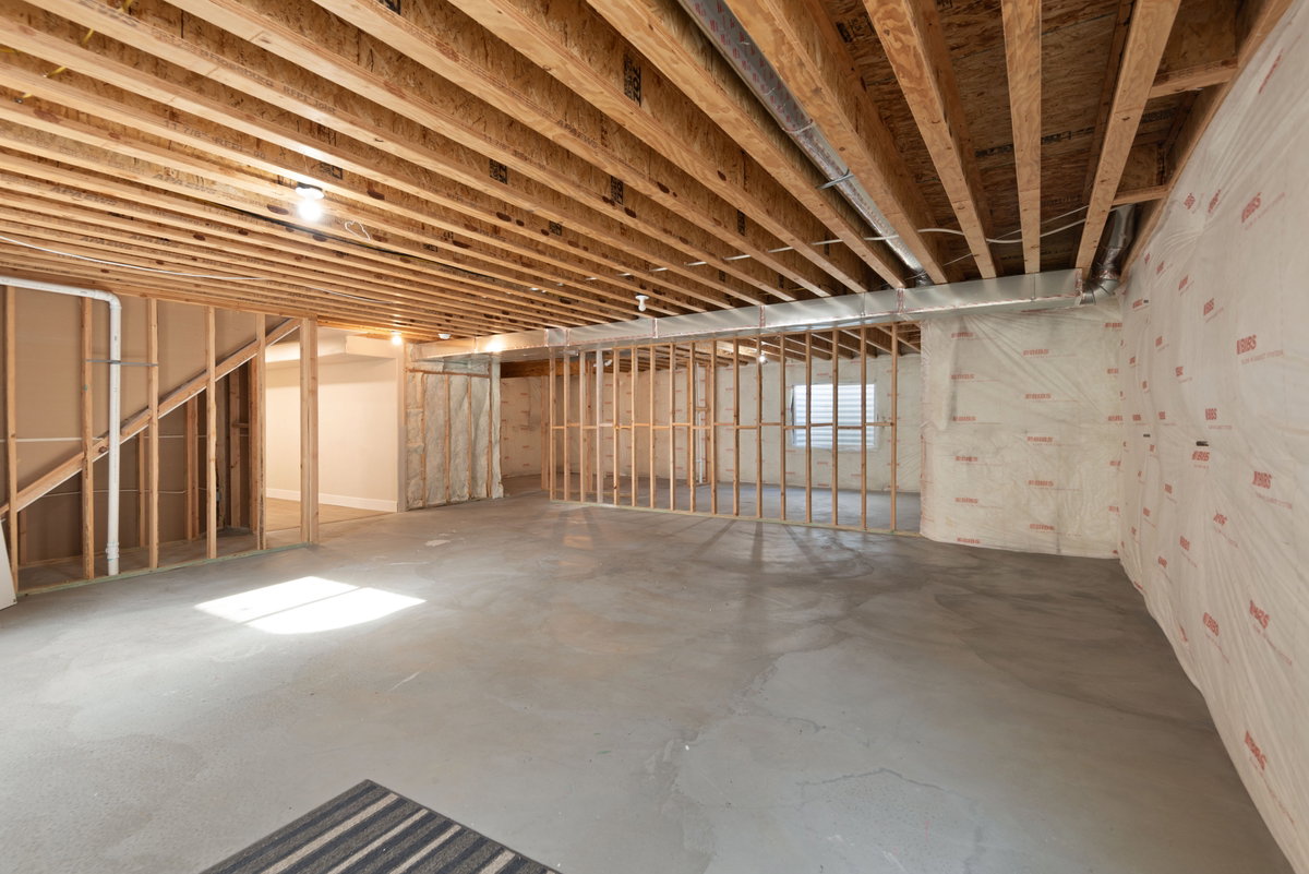 Unfinished basement featuring exposed wood joists, concrete flooring, and framed partition walls
