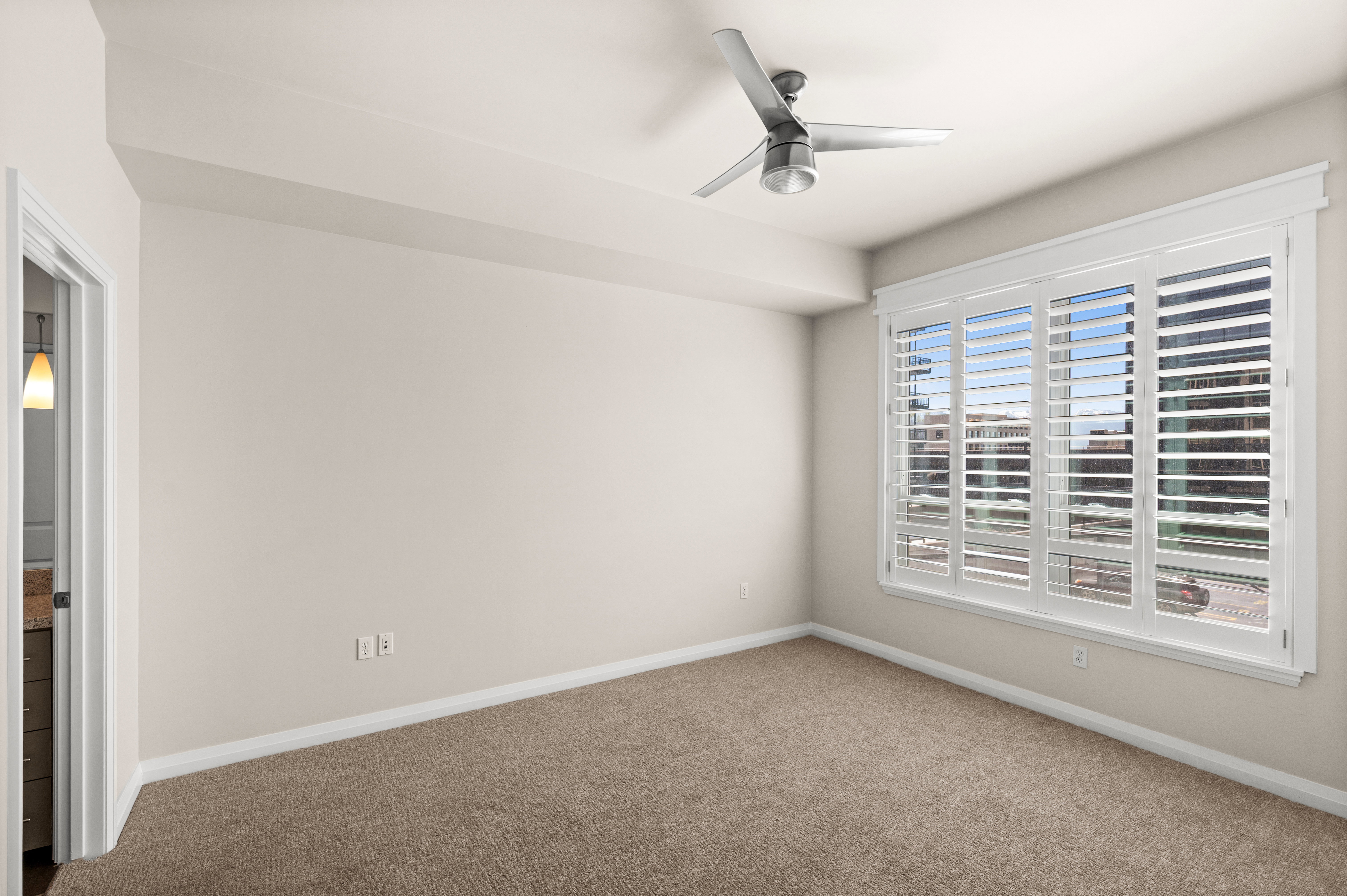 Carpeted room featuring a large window with white plantation shutters, a ceiling fan, and neutral wall tones