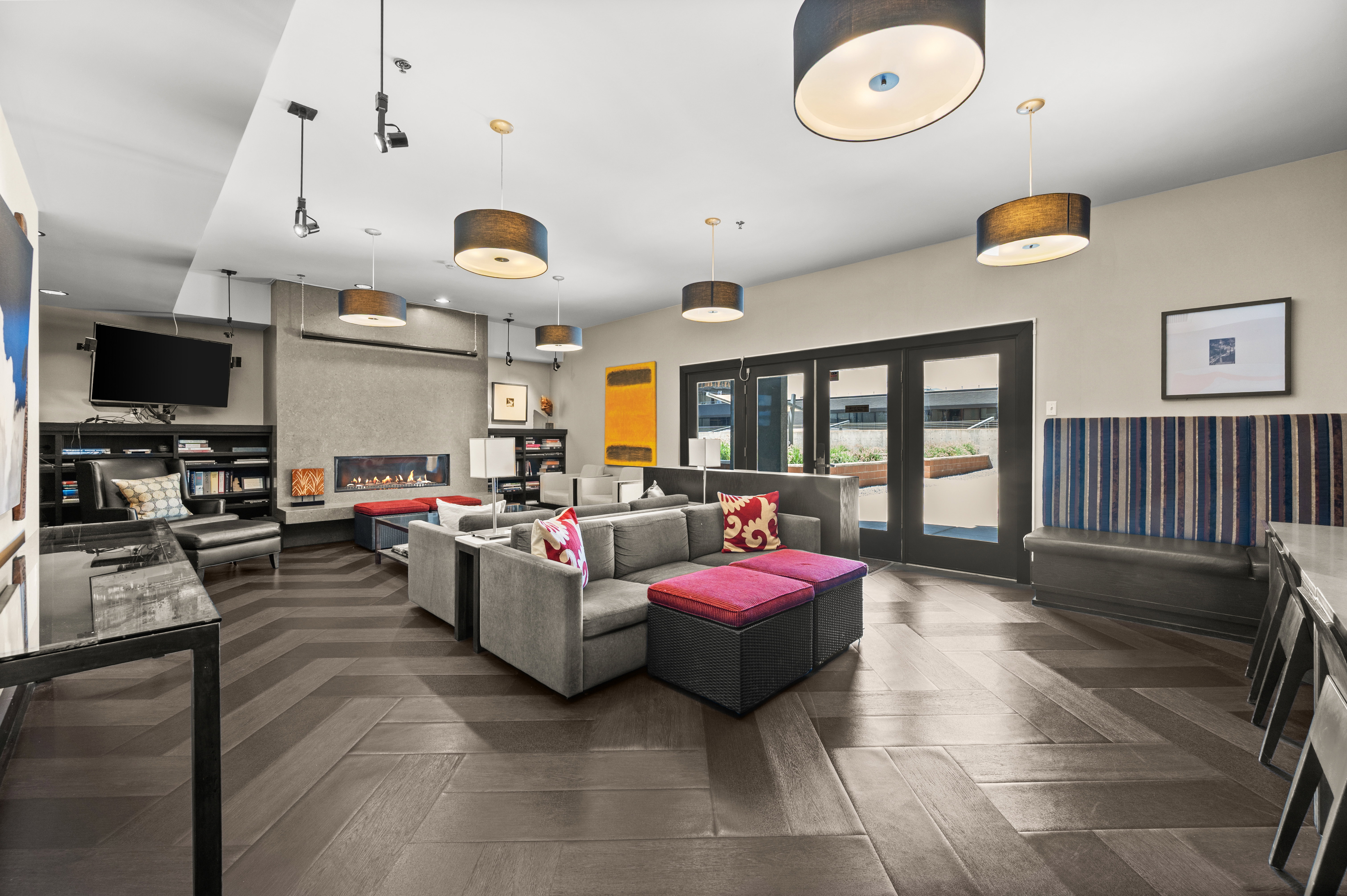 Spacious gathering room featuring wood-finish flooring with a herringbone pattern, a built-in linear fireplace, and multiple drum pendant lights