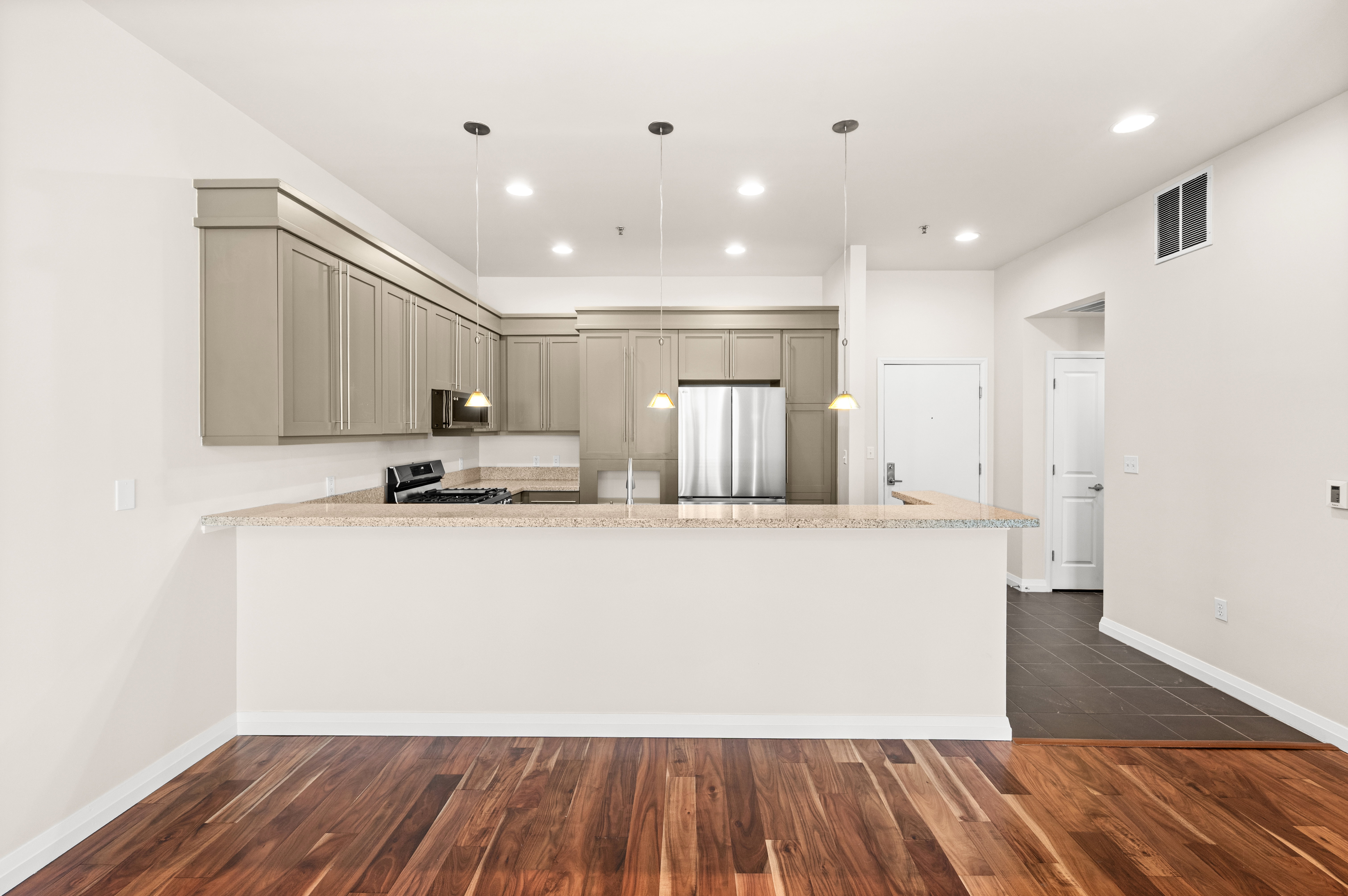 Modern kitchen featuring light gray cabinetry, stainless steel appliances, granite-style countertops, and pendant lighting